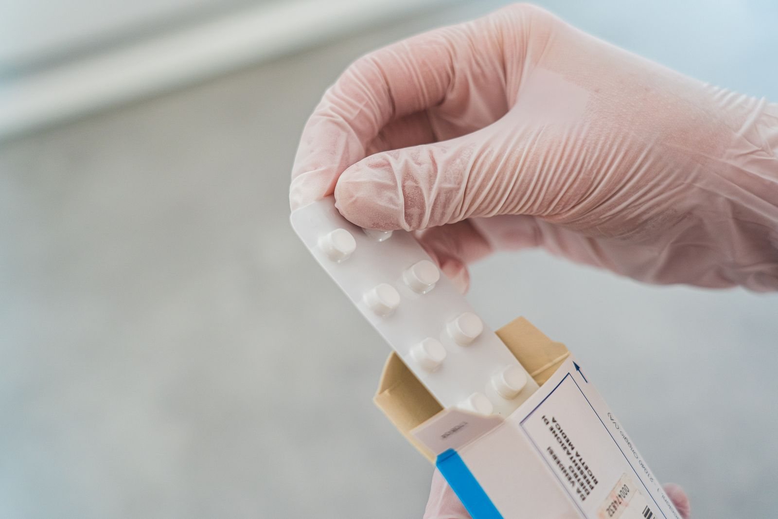 A hand holds a medication box in front of a light wall