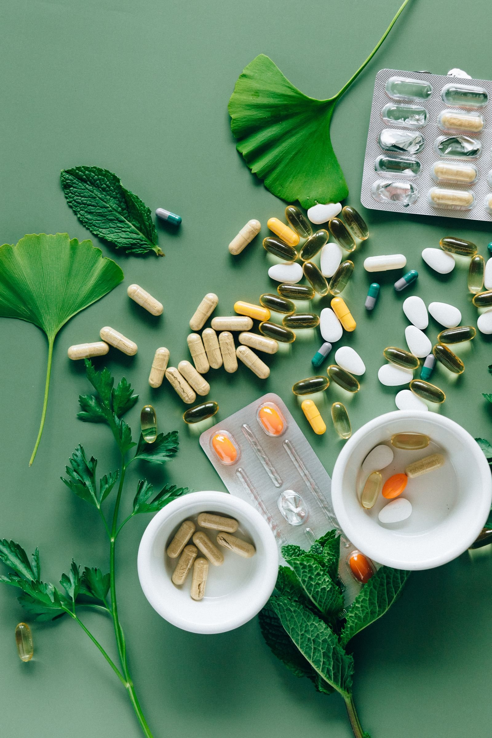 Capsules and tablets arranged on a green background with leaves