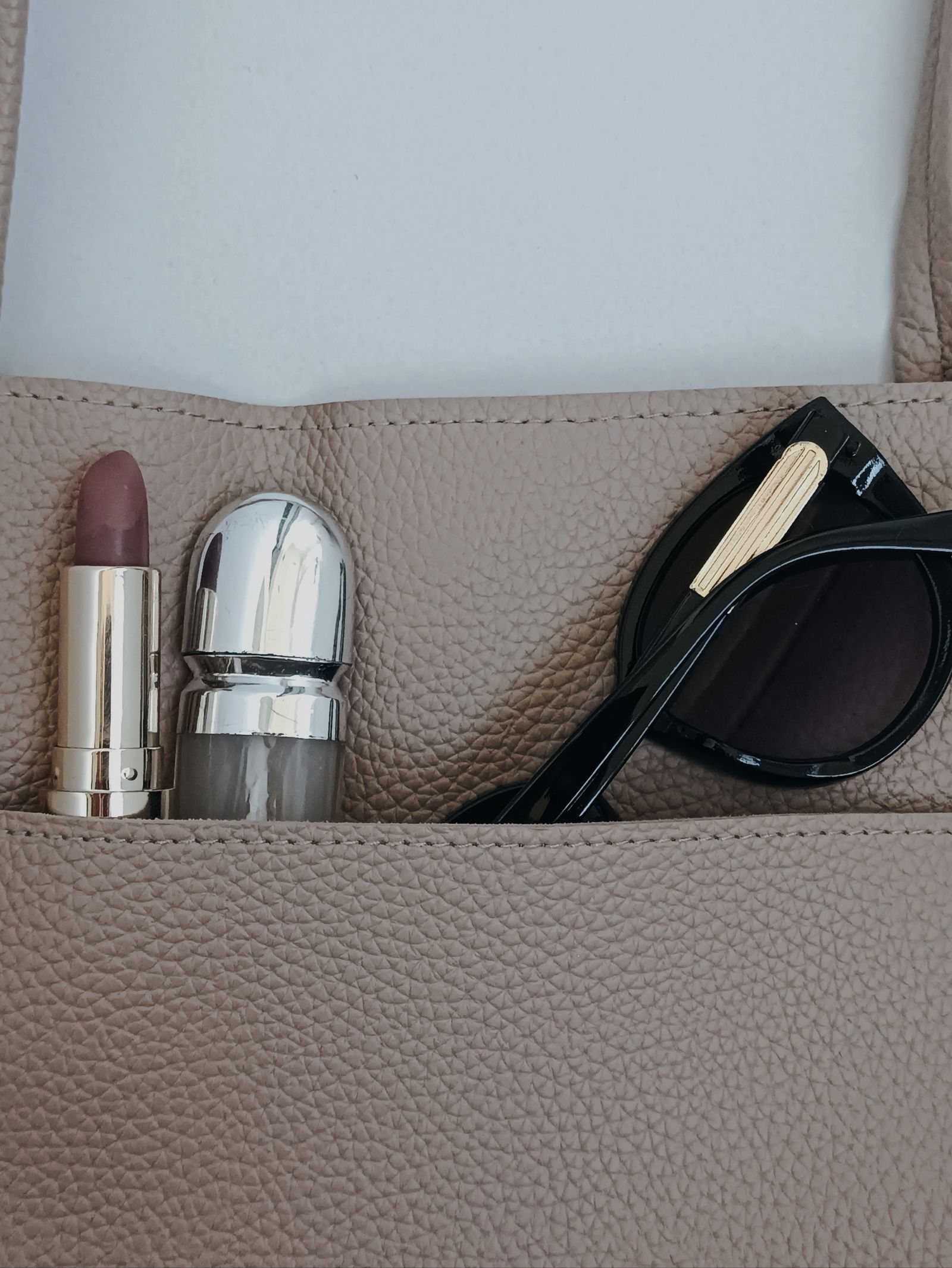 An open handbag, a blister pack, lipstick and sunglasses